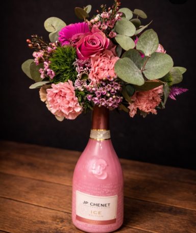 Ein Blütenstrauß aus pinken und grünen Blumen in einer dekorierten Flasche.