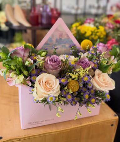 Bunte Blumenarrangement in einer rosa Verpackung mit einem dekorativen Element.