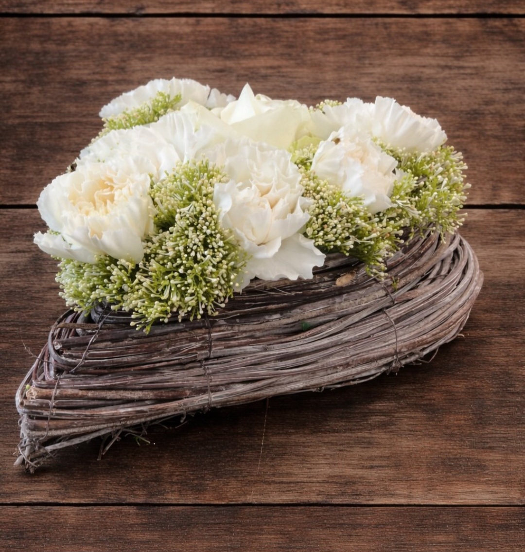 Plantula Amedorf - Trauerkränze Arrangement aus weißen Blumen und grünem Blattwerk in einem geflochtenen Korb.