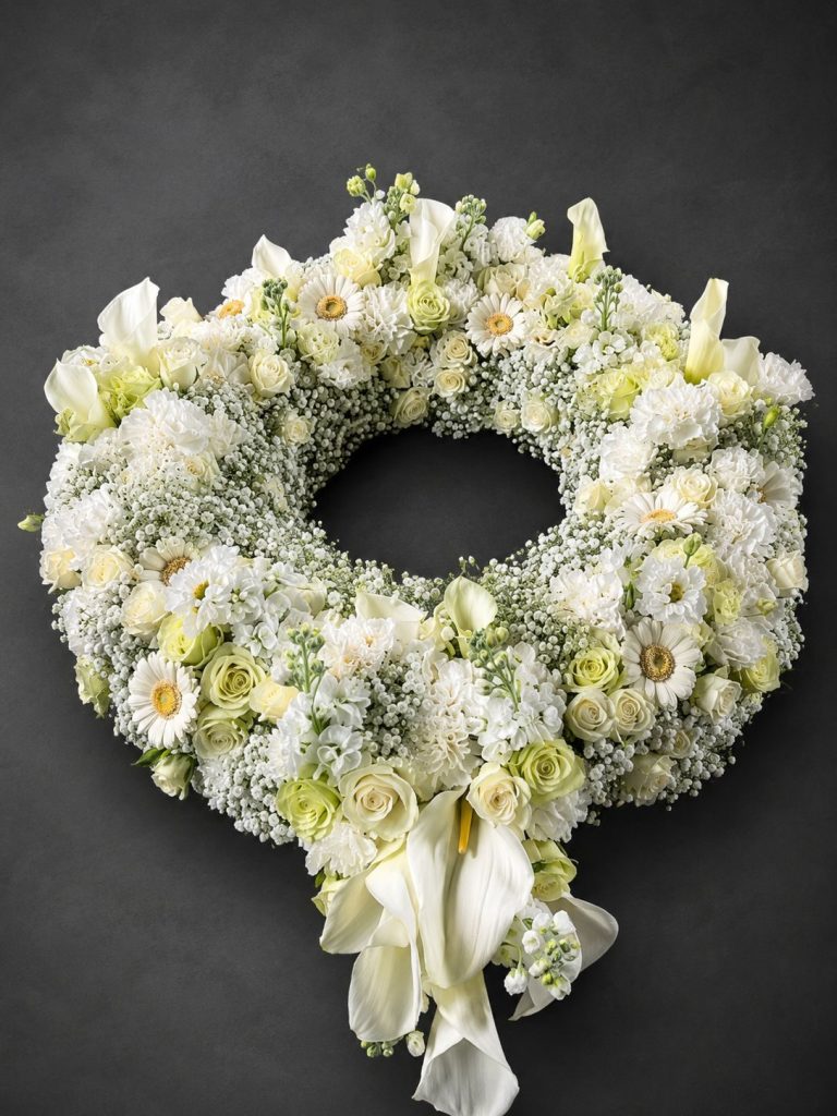 Plantula Amedorf - Trauerfloristik Trauergesteck - Kreisförmiger Blumenkranz aus weißem und grünem Blumenschmuck mit Schleife.