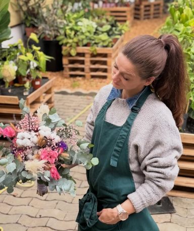 Frau mit einem Strauß aus bunten Blumen in einem Gewächshaus.