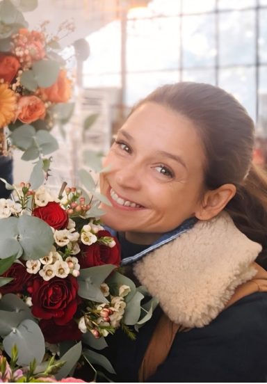 Lächelnde Frau hält einen Blumenstrauß mit roten und weißen Blumen in der Hand.